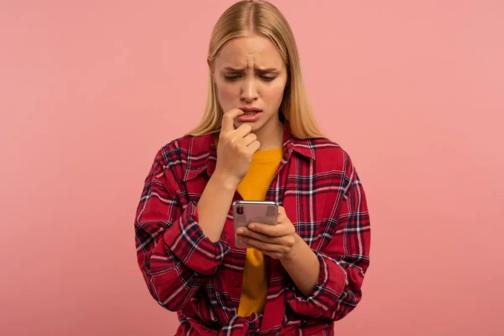 Uma garota ansiosa roendo sua suas unhas enquanto vê seu celular