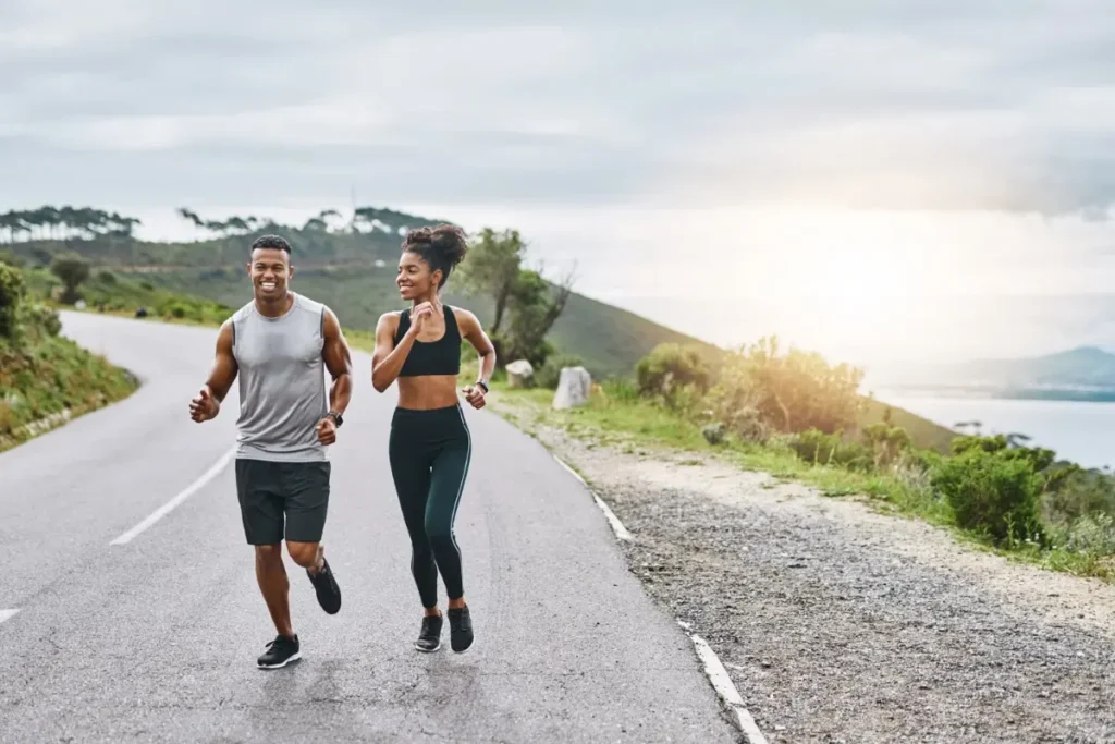 Duas pessoas correndo ao ar livre em uma estrada, sorrindo e aproveitando o momento.