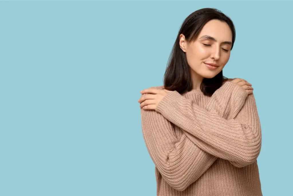 Mulher abraçando a si mesma com expressão serena, transmitindo amor próprio e acolhimento.