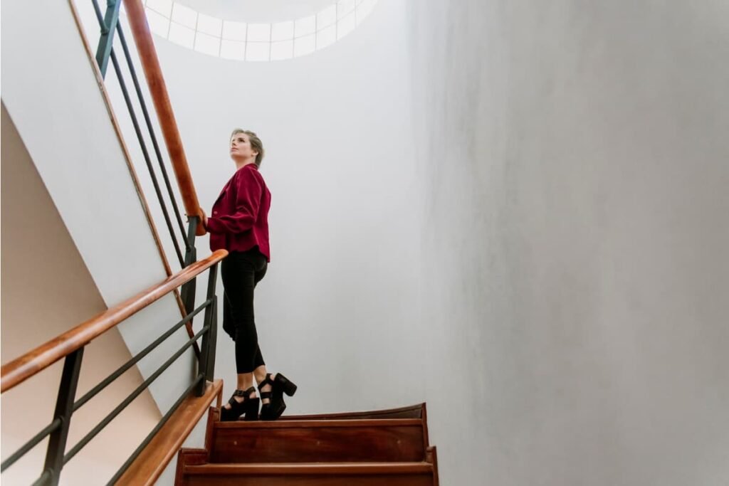 Mulher subindo uma escada de madeira enquanto olha para cima, simbolizando crescimento e evolução pessoal.